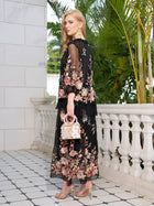 A woman stands on a tiled balcony in the Social Queen Floral Embroidery 100% Mulberry Silk Tulle Skirt, gold heels, and holding a white floral handbag, with green foliage and a white stone railing in the background.