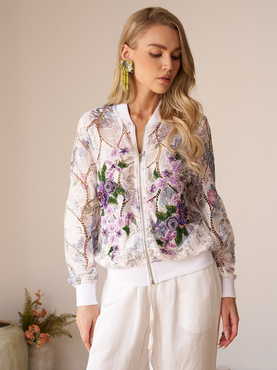 A woman indoors, head slightly tilted down, wears the Social Queen Floral Embroidery Lace Cutout Jacket paired with white pants.