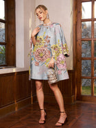 Indoors, a woman wears the Social Queen Floral Jacquard Beaded Jacket in light blue, paired with high-heeled sandals and a metallic handbag. She poses by wooden windows and paneling.