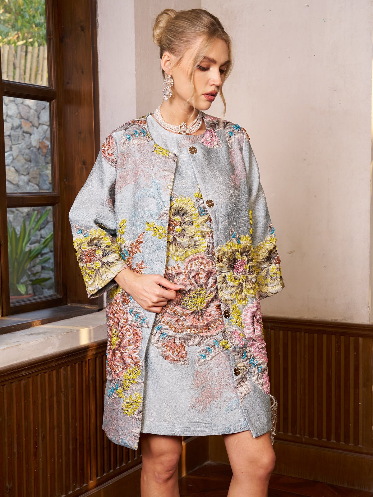 A woman stands indoors wearing the Social Queen Floral Jacquard Beaded Jacket and matching dress, her hair in an updo and hands resting on the jacket.