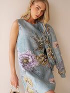 A woman in the Social Queen Floral Jacquard Dress with a matching jacket draped over her shoulder and a beaded bag poses against a neutral wall—a stunning wedding guest look.