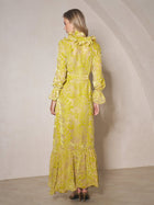 A woman stands indoors with her back to the camera, wearing the Social Queen Floral Jacquard Velvet Ruffles Dress—a long wedding guest dress with ruffled details, long sleeves, and a wrap silhouette—paired with high-heeled shoes.
