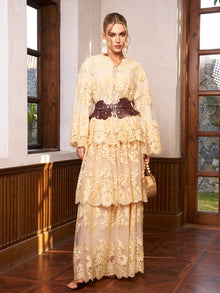 A woman stands indoors wearing the Social Queen Floral Lace Embroidered Blouse in beige, styled with a wide dark brown belt, earrings, and a small wicker handbag.