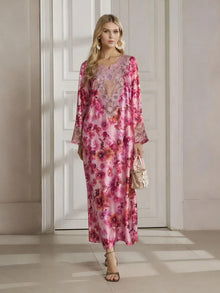 A woman stands indoors in the Social Queen Floral Print Beaded Dress, featuring a long silhouette with a botanical pattern and delicate beadwork, paired with a small handbag and heeled sandals.
