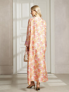 A woman stands indoors facing a white door, wearing the Social Queen Floral Print Beaded Dress and heeled sandals, holding a small transparent handbag, with her back to the camera.