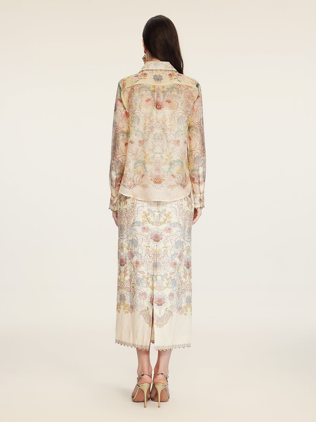 A woman stands facing away, wearing the Social Queen Floral Print Collared Blouse with matching skirt and heeled sandals.