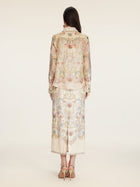 A woman stands facing away, wearing the Social Queen Floral Print Collared Blouse with matching skirt and heeled sandals.