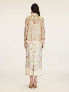 A woman stands facing away, wearing the Social Queen Floral Print Collared Blouse with matching skirt and heeled sandals.