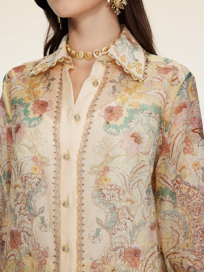 A woman wears the Social Queen Floral Print Collared Blouse, detailed with gold buttons and ornate trim, paired with a gold necklace and earrings.