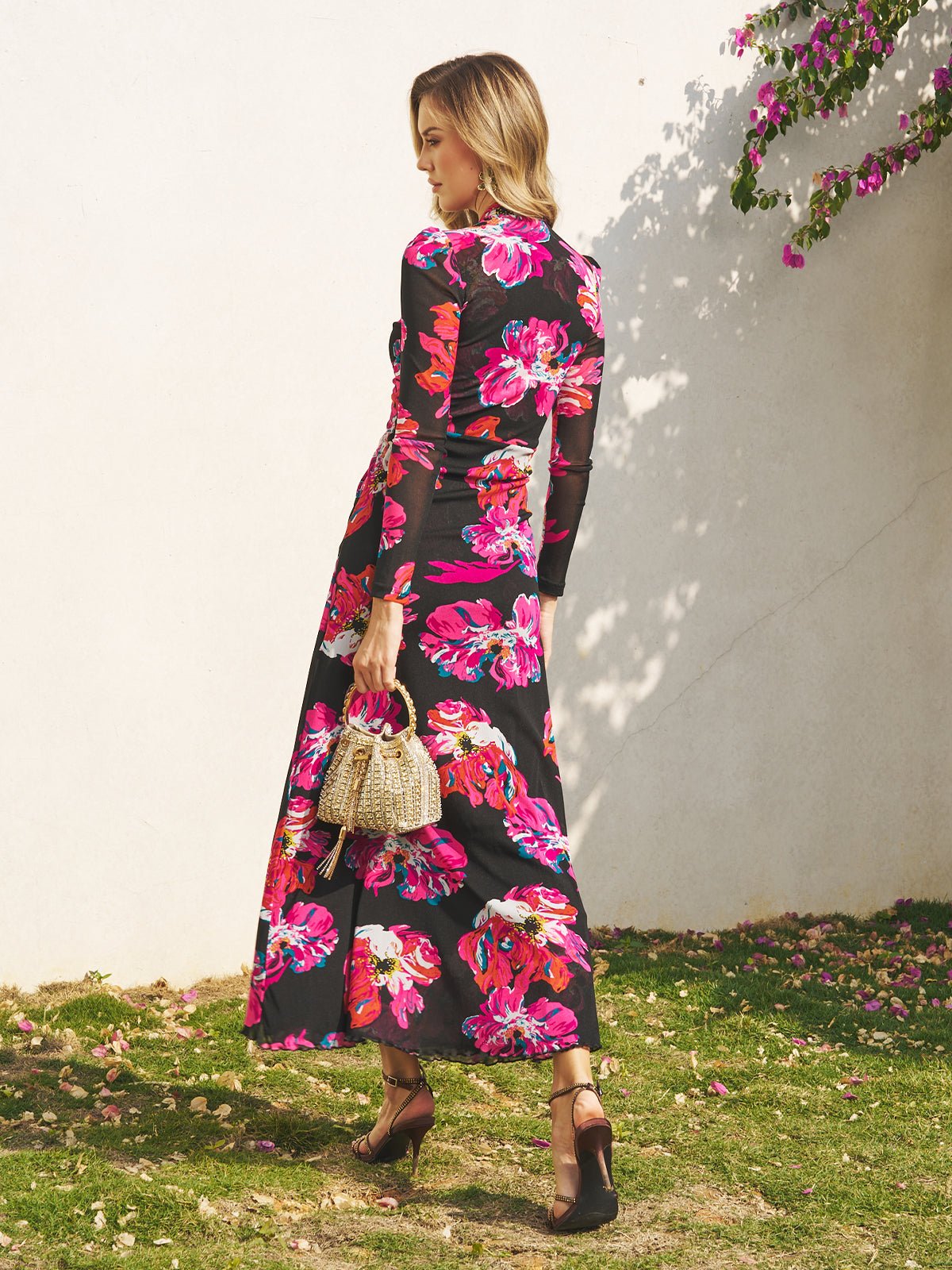 A woman stands outdoors in sunlight, wearing the Social Queen Floral Print Knot Front Knit Dress, holding a woven handbag and pairing the look with black heels.