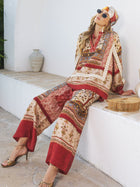 A woman in Social Queen’s Floral Print Wide-Leg Boho Pants, headscarf, and sunglasses sits on a white ledge with a wooden handbag nearby.