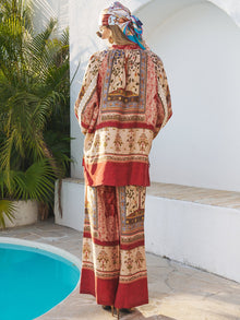 Wearing Social Queen’s Floral Print Wide-Leg Boho Pants and a headscarf, a person stands by a pool with white walls and greenery, facing away.