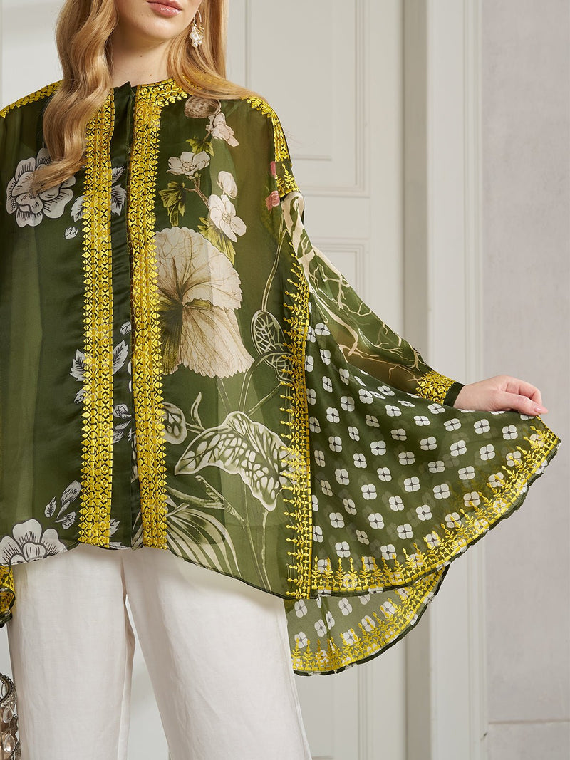 A woman models the Social Queen Floral Printed Embroidered 100% Silk Blouse—green with a sheer finish, gold-thread embroidery, and yellow trim—paired with white pants and showcasing the sleeve’s detailed fabric.
