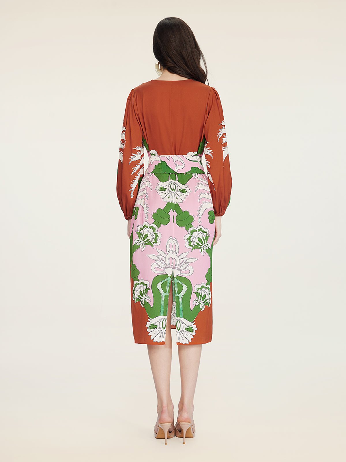A woman faces away, radiating vacation elegance in the Social Queen Floral Printed Silk Dress, featuring a pink, green, and white floral print, paired with beige heels against a plain background.