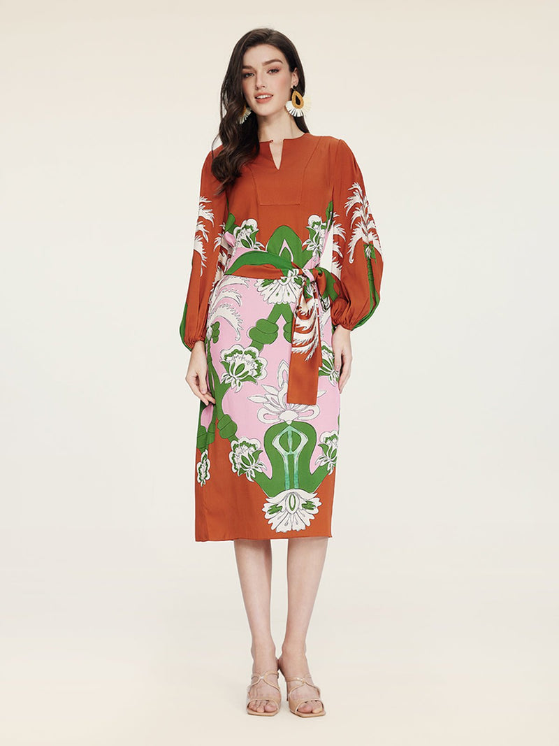 A woman wears the Social Queen Floral Printed Silk Dress in rust with green, pink, and white blooms, styled with beige sandals and statement earrings for vacation elegance.