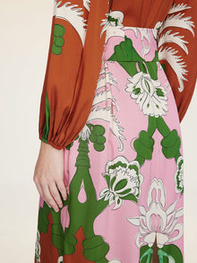 A person stands with their left arm relaxed by their side, wearing the Social Queen Floral Printed Silk Dress featuring pink, green, white, and rust-colored floral prints that evoke vacation elegance.