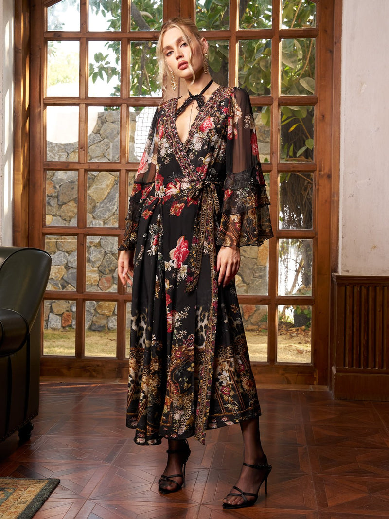 A woman poses in a sunlit room before large wooden-framed windows, wearing the Social Queen Floral Printed Silk Ruffle Dress with sheer sleeves and black strappy heels.