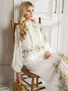 A woman wears the Social Queen Floral Printed Stand-Collar Dress as she sits on a wooden chair, holding a wooden handbag against a neutral background with white paneled doors.