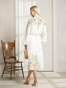 A woman faces away indoors, holding a small rattan handbag and wearing the Social Queen Floral Printed Stand-Collar Dress. A wooden chair stands nearby.