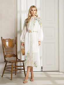 A woman stands indoors by a wooden chair in the Social Queen Floral Printed Stand-Collar Dress, holding a wicker handbag and wearing sandals—the perfect go-to spring vacation outfit.