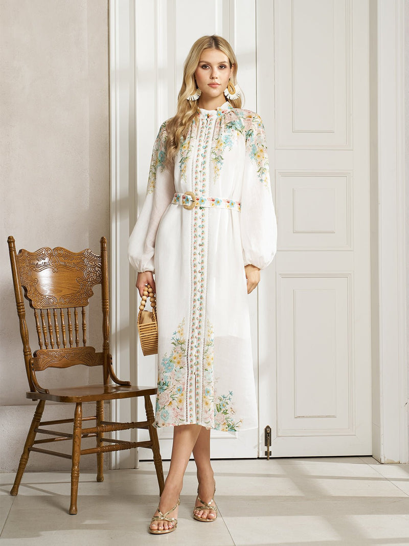 A woman stands indoors by a wooden chair in the Social Queen Floral Printed Stand-Collar Dress, holding a wicker handbag and wearing sandals—the perfect go-to spring vacation outfit.