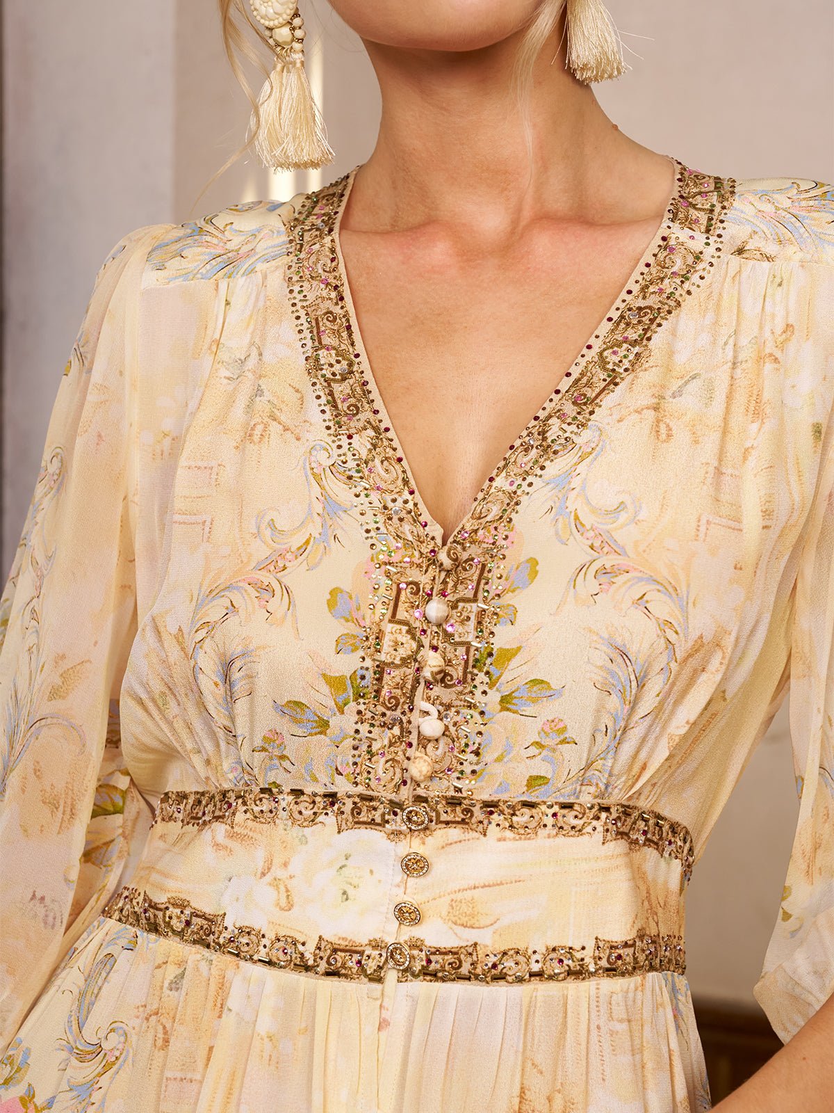 A close-up of a woman wearing the Social Queen Floral Silk V-Neck Beaded Dress, featuring floral print, decorative trim, ornate buttons, and a matching embellished belt—perfect for a stylish wedding guest. Her face is partially out of frame.