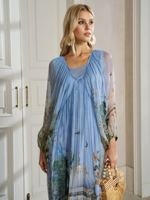 A woman in the Social Queen Garden-Inspired Print Pleated Dress holds a wooden handbag while standing indoors near white cabinets.