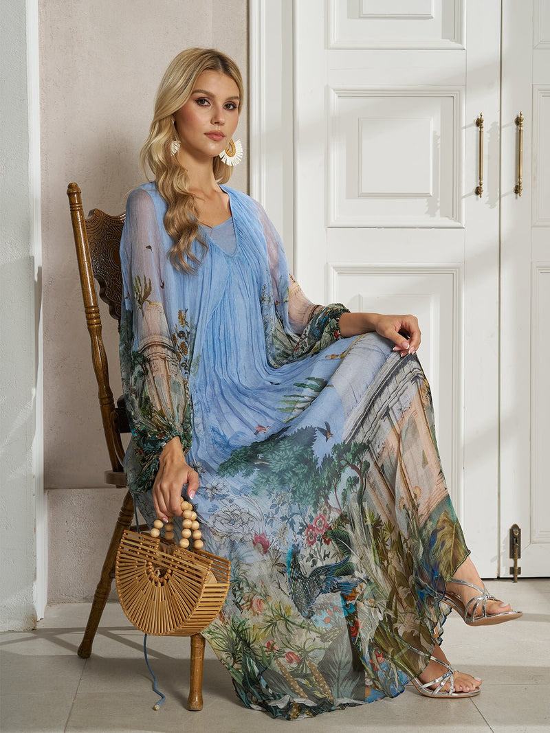 A woman sits on a wooden chair in front of white paneled doors, wearing the Social Queen Garden-Inspired Print Pleated Dress and holding a woven bamboo handbag.