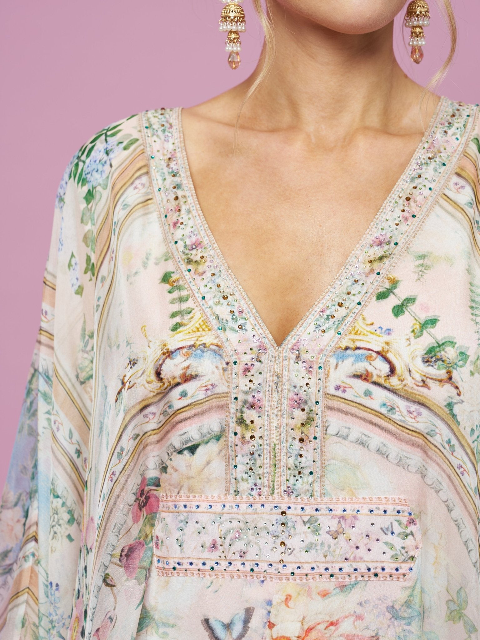 A close-up of a woman wearing the Social Queen Garden Print Silk Dress against a pink background, with earrings visible.