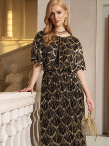 A woman wearing the Social Queen Gilded Beaded Cape Dress stands indoors by a stone railing, holding a gold handbag, with statues and architectural details in the background.