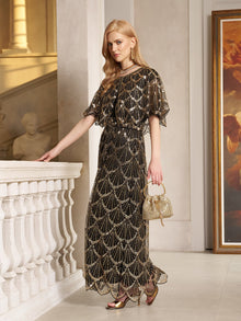 A woman wears the Social Queen Gilded Beaded Cape Dress indoors by a white railing, holding a small gold purse and sporting metallic heels.