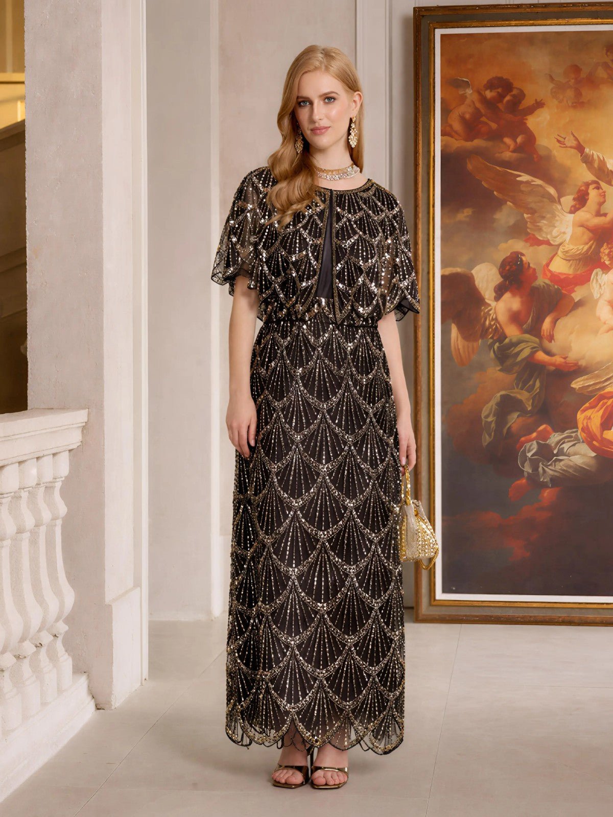 A woman in the Social Queen Gilded Beaded Cape Dress poses indoors by a framed angel painting, holding a small gold purse and wearing statement earrings.