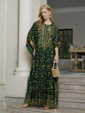 A woman indoors holds a woven handbag, wearing the Social Queen Gold Sequin Beaded Tulle Cape Dress. A set dining table and chairs are visible in the background.