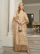 A woman stands on indoor steps wearing the Social Queen Gold Sequin Beaded Tulle Cape Dress and holding a matching purse, with a dining room in the background.
