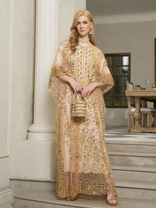 A woman stands on indoor steps wearing the Social Queen Gold Sequin Beaded Tulle Cape Dress and holding a matching purse, with a dining room in the background.