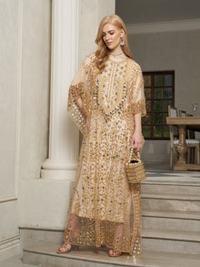 A woman wearing the Social Queen Gold Sequin Beaded Tulle Cape Dress stands on marble steps indoors, accessorizing with a small gold bag and statement earrings.