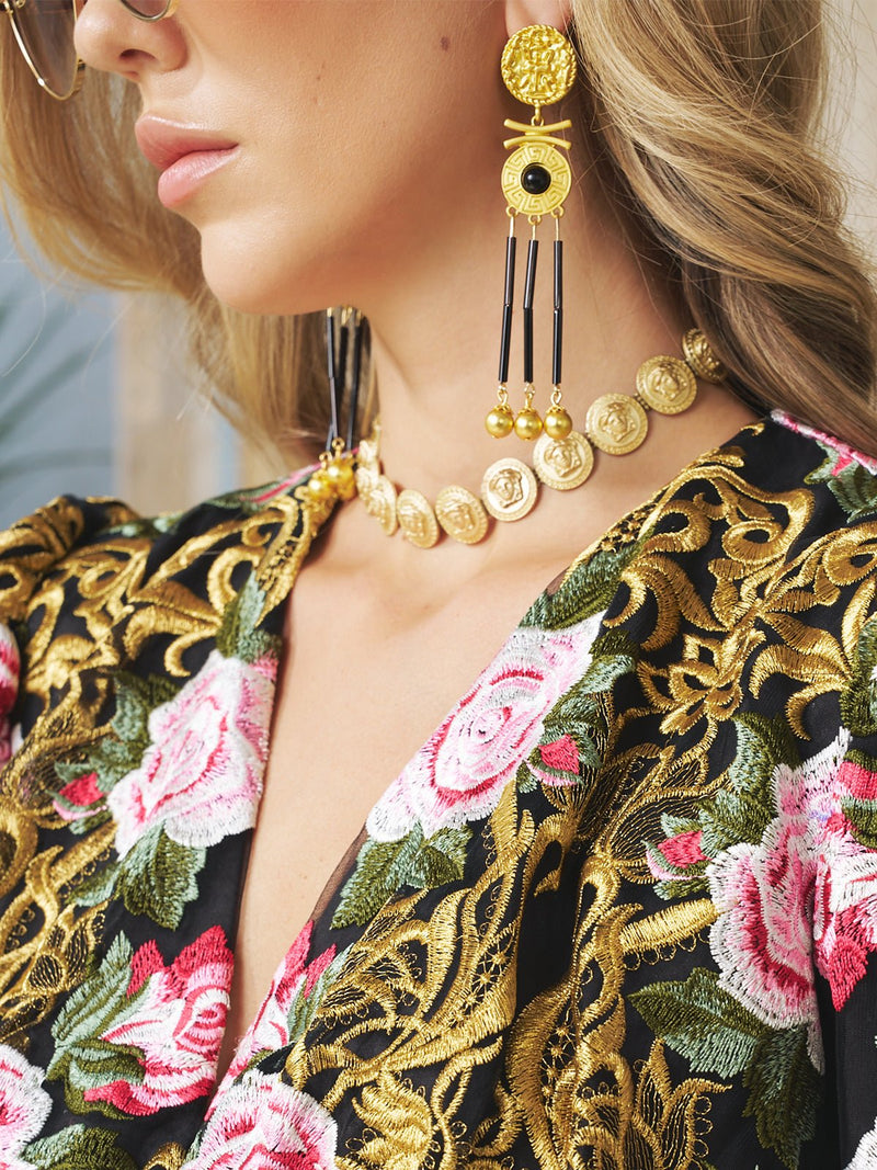 Close-up of a woman wearing Social Queen Gold-Tone Tassel Earrings and a floral embroidered dress with pink roses and gold leaves.