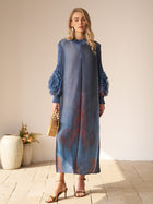 Indoors, a woman wears the Social Queen Gradient Pleated Dress with 3D Floral Sleeves—ideal for a wedding guest. She accessorizes with a wicker handbag and heeled sandals.