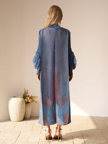 A woman stands indoors facing away, wearing Social Queen's Gradient Pleated Dress with 3D Floral Sleeves and heels—ideal for a wedding guest. Two ceramic vases with flowers sit to her left on the floor.