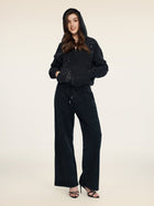 A person stands facing forward in Social Queen's Gradient Rhinestone Wide-Leg Pants with an elastic waist, a black hooded zip-up jacket, and black high-heeled sandals.