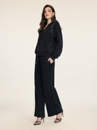 A woman poses against a plain background wearing Social Queen’s Gradient Rhinestone Wide-Leg Pants with an elastic waist and subtle cutouts, styled with a black hoodie and black high-heeled sandals.