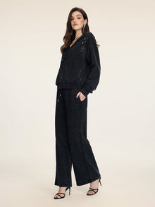 A woman poses against a plain background wearing Social Queen’s Gradient Rhinestone Wide-Leg Pants with an elastic waist and subtle cutouts, styled with a black hoodie and black high-heeled sandals.