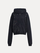 The Social Queen Hand-Applied Rhinestone Washed Hoodie is a relaxed black zip-up with a hood, side pockets, and multicolored hand-applied rhinestones scattered across the chest and sleeves.