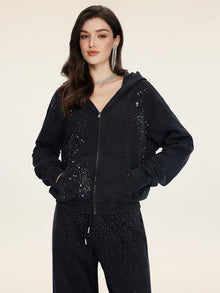 A woman models the Social Queen Hand-Applied Rhinestone Washed Hoodie with matching pants, both in black and embellished with sparkling hand-applied rhinestones, set against a plain light background.
