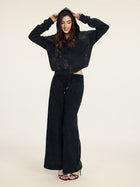 A woman faces forward in the Social Queen Hand-Applied Rhinestone Washed Hoodie with matching wide-leg pants, finished with black heeled sandals.