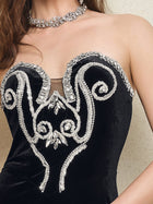 A person wears the Social Queen Hand-Applied Silver Crystal Baroque Velvet Gown, a strapless fitted evening dress featuring hand-beaded silver crystal swirl details, paired with a coordinating jeweled necklace.