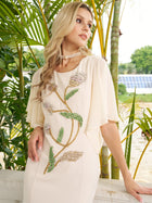 A woman wearing the Social Queen Hand-Beaded Floral Mermaid Dress with chiffon cape sleeves stands near green plants, looking to the side.