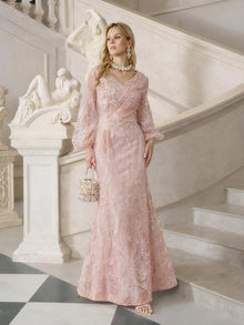 A woman wears the Social Queen Hand-Beaded Lace Mermaid Dress in pink on marble stairs, holding a small embellished handbag, with classical statues in the background.