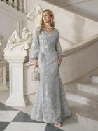 A woman in the Social Queen Hand-Beaded Lace Mermaid Dress stands on a marble staircase by a sculpture, holding a handbag and wearing statement jewelry.