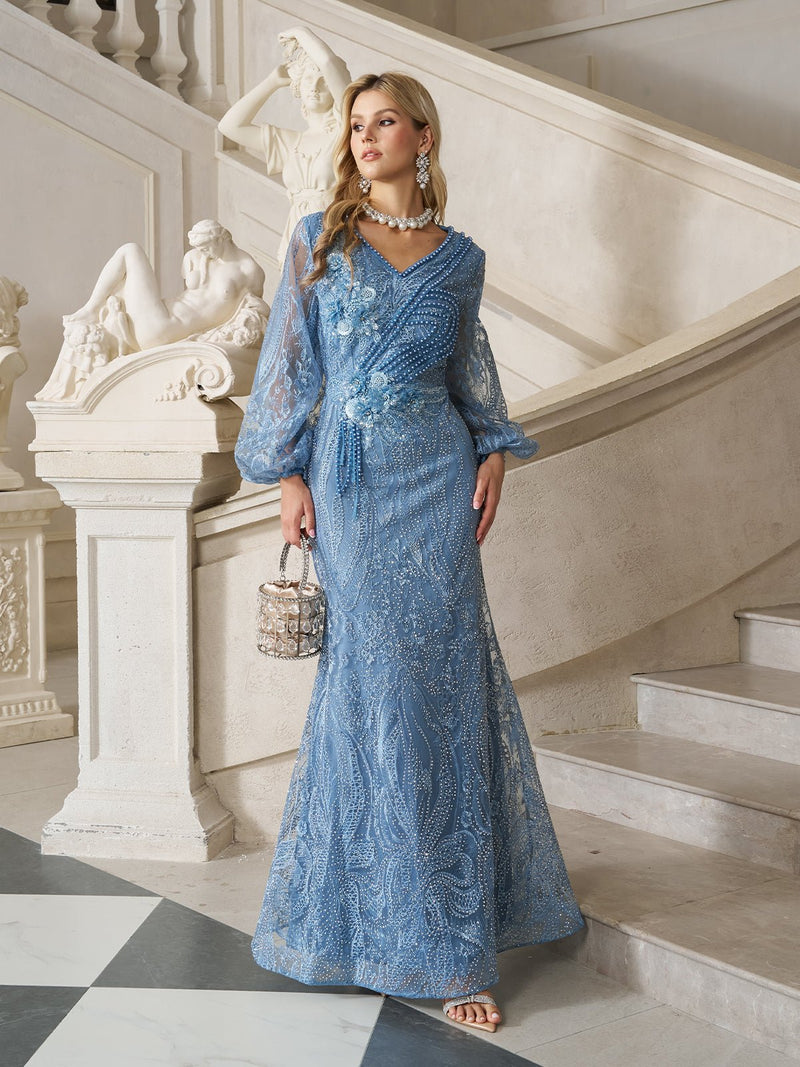 A woman in the Social Queen Hand-Beaded Lace Mermaid Dress stands on marble flooring by a staircase and classical sculptures, holding a small handbag.